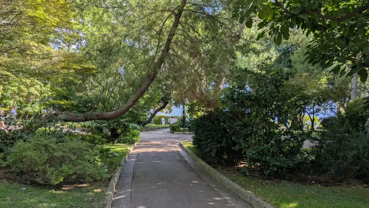 Shaded path through the Saint-Martin Gardens in Monaco, with Mediterranean planting and the sea beyond